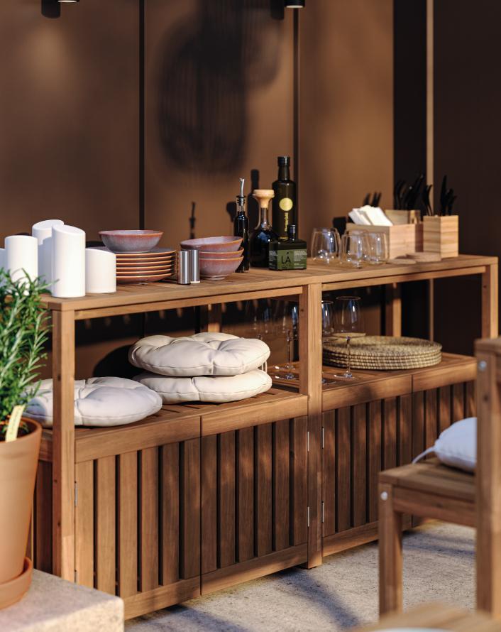 Wooden storage cabinet with stacked cushions, dishes, bottles, glasses, and kitchen accessories.