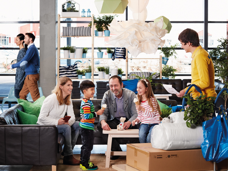 People sitting in a modern living room with boxes and a staff member assisting.