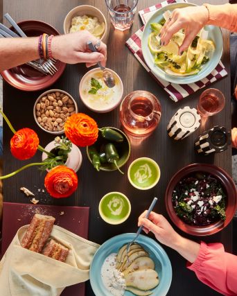Una toma desde arriba de una mesa de comedor con personas comiendo de los cuencos y platos SPJUTLILJA y bebiendo de las tazas amarillas.