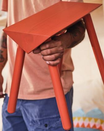 Persona sosteniendo una mesa auxiliar roja con patas inclinadas.