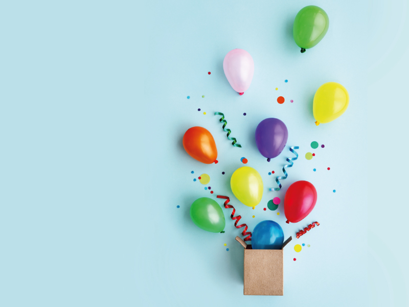 Colorful balloons rising from a box against a light blue background.