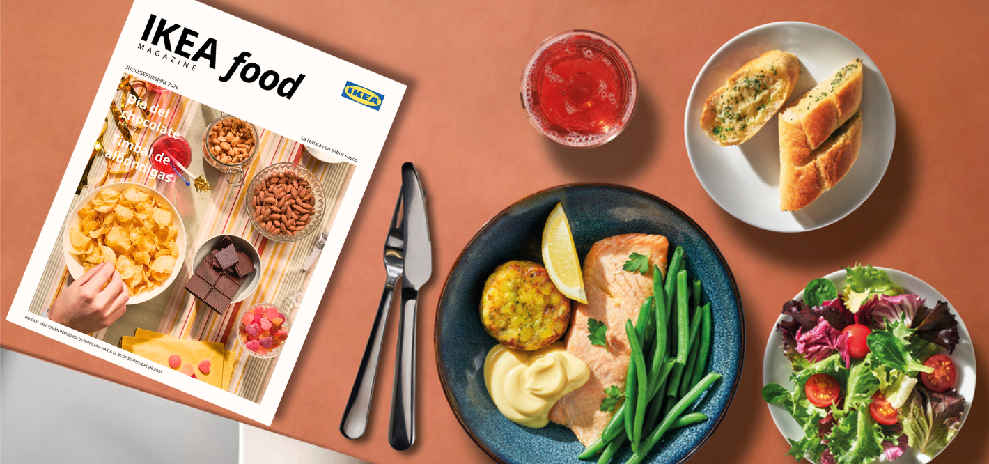 Top-down view of a table featuring the "IKEA food magazine", cutlery, a plate of salmon with green beans, a fresh salad, garlic bread, and a drink.