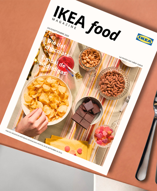 Close-up of the "IKEA food magazine" cover on a terracotta table, featuring snacks like potato chips, chocolate bars, and mixed nuts.