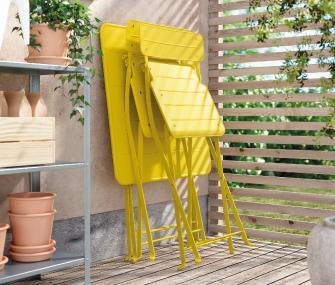 Conjunto de sillas plegables amarillas apiladas en un balcón o terraza junto a plantas.