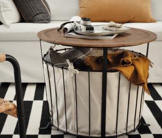 Round bedside table with a glass, a yellow notebook, and a decorative speaker beside a bed.