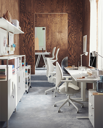 Modern office setting with white desks and chairs against wood-paneled walls.