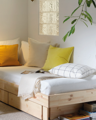 Banco de madera con cojines en tonos neutros y amarillos, acompañado de una manta decorativa en un espacio luminoso y acogedor.