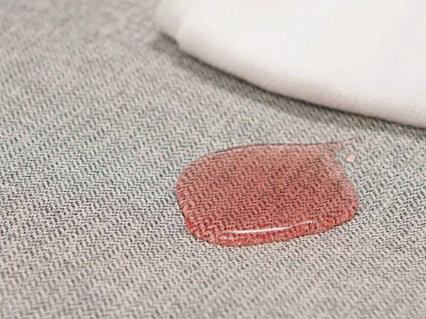 Spilled liquid droplet resting on water-resistant gray fabric next to a cloth.