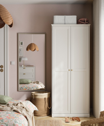 Dormitorio luminoso con armario blanco, espejo de cuerpo entero y textiles florales.