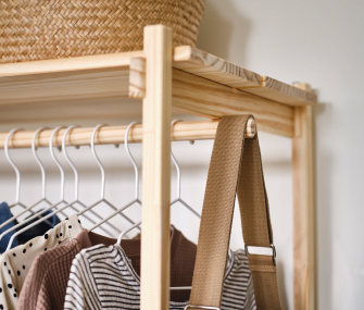 Perchero de madera con ropa colgada, cesta de mimbre y correa beige.