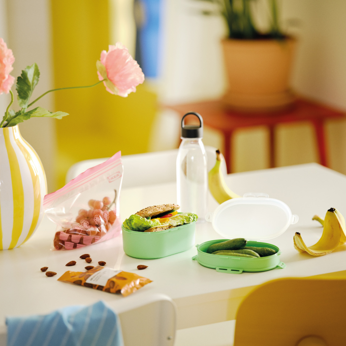 Mesa con recipientes de comida, botella reutilizable, frutas y snacks.