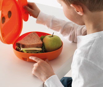Lonchera naranja abierta con sándwich y manzana sobre una mesa.