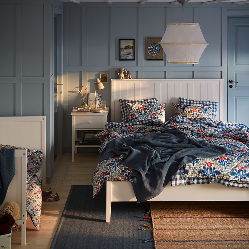 A blue bedroom with a white GULLABERG bed with floral bed linen, a blue throw and a white bedside table.