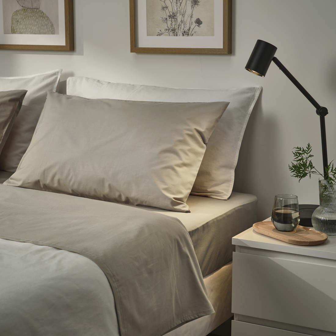 Cama con ropa de cama beige, lámpara negra y mesa de noche minimalista.