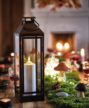 Black lantern with a lit candle on a table decorated with natural accents.