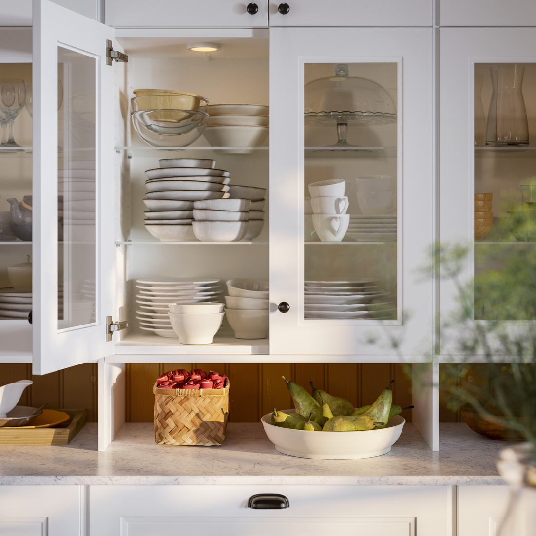 Vitrina de cocina blanca con vajilla organizada y un frutero con peras sobre la encimera.