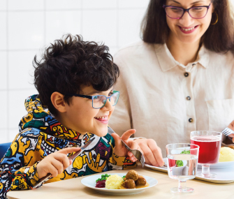 Persona joven comiendo albóndigas suecas junto a otra persona en una mesa.