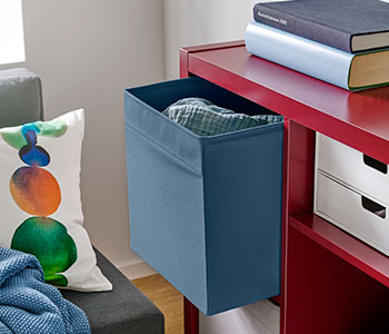 A living room with a blue DRÕNA box placed on a red shelf, beside a green and white patterned cushion.