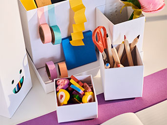 Organizador de escritorio blanco con lápices, tijeras, cintas decorativas y gomas de borrar.