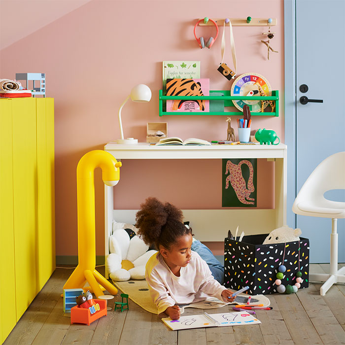 Niña dibujando en el suelo de una habitación infantil colorida frente a un escritorio blanco.