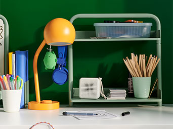 Yellow lamp and green shelf with pencils on a desk against a green wall.
